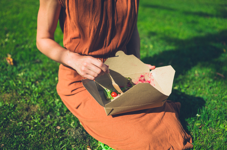 A young woman is eating a take away salad in the parkの写真素材