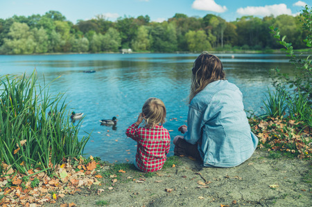 A mother and a toddler are relaxing by a pond in the forest on a sunny autumn dayの写真素材