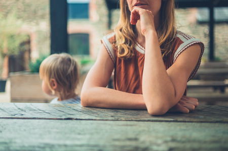 A young mother and her toddler are sitting outside at a tableの写真素材