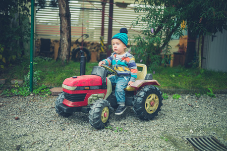 A little toddler is riding on a toy tractorの写真素材