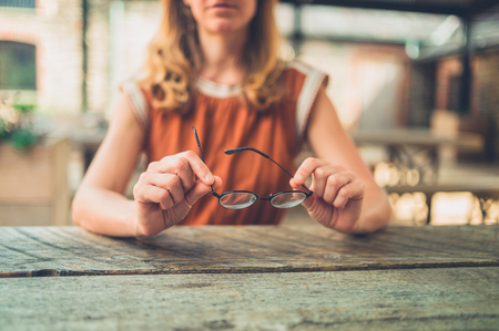 A young woman is sitting at a table outside with a pair of glassesの写真素材