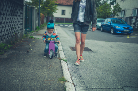 A mother is walking in the street next to her toddler who is riding a tricycleの写真素材