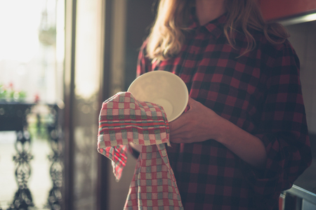 A young woman is drying the dishes in her kitchenの写真素材