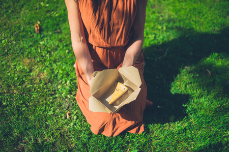 A young woman is sitting on the grass with a piece of cake in a boxの写真素材