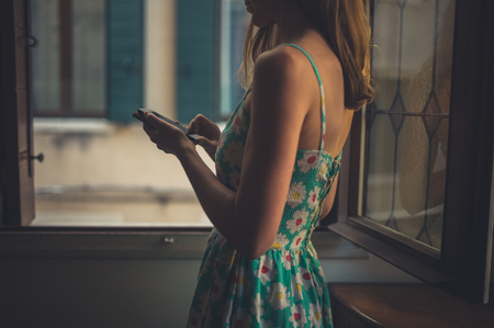 A young woman is using a smart phone at home at sunsetの写真素材