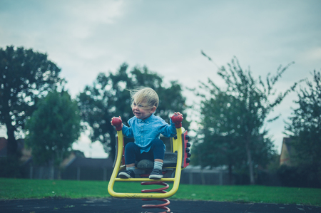 A little toddler is sitting on the play equipment at a playgroundの写真素材