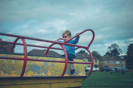 A little toddler is sitting on the play equipment at a playgroundの写真素材