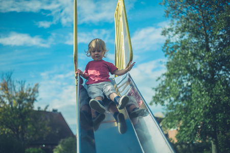 A little toddler is coming down the slide at a playgroundの写真素材