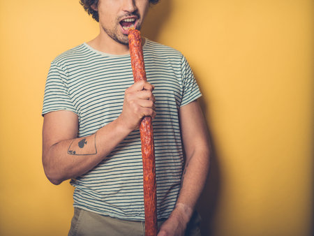 A young man is about to put a very big sausage in his mouthの写真素材