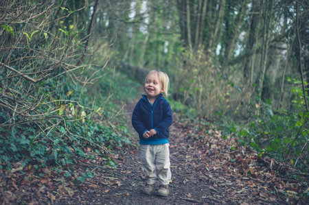 A little toddler is standing on a path in the woods
