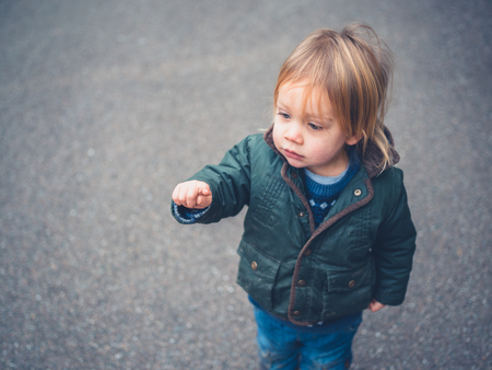 A little toddler is standing in the road and is pointingの写真素材