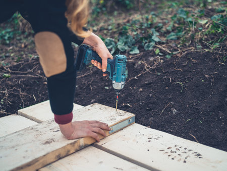 A young woman is using an impact driver outdoors in the winter