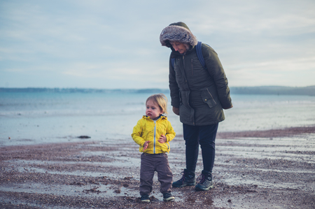 A little toddler is walking on the beach in winter with his grandmotherの写真素材