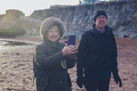 A senior couple are taking photos with a smartphone on the beach in winterの写真素材