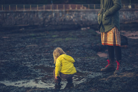 A young mother and her toddler are on the beach in winter