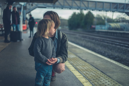 A young mother and her toddler are waiting for the train on a platform