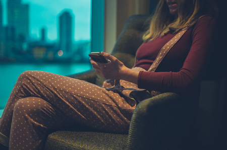 A young woman is using her smartphone by the window in a city apartmentの写真素材