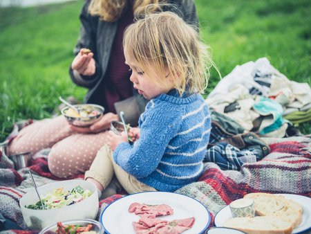 A young mother and her toddler are enjoying a picnic on the grass in springの写真素材