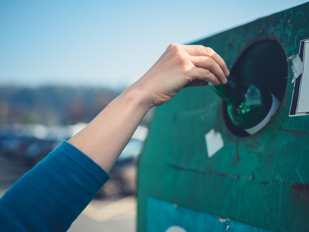 A young woman is recycling a glass bottle at a bottle bankの写真素材