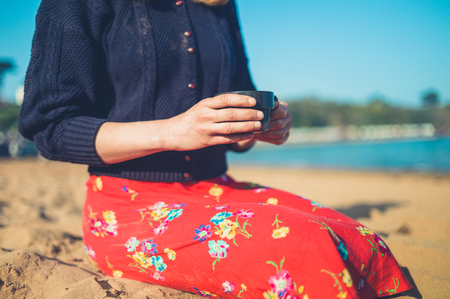 A young woman is drinking coffee on the beachの写真素材