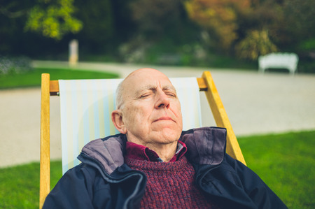 A senior man is relaxing in a deck chair outdoorsの写真素材