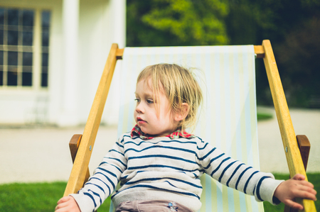A little toddler is sitting in a deck chair outdoorsの写真素材
