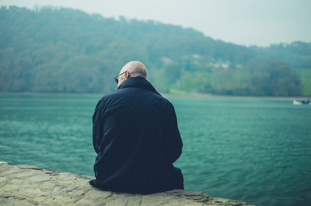 A senior man is sitting by the riverの写真素材