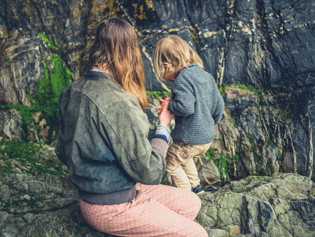 A young mother and her toddler are exploring the rocks on the beachの写真素材