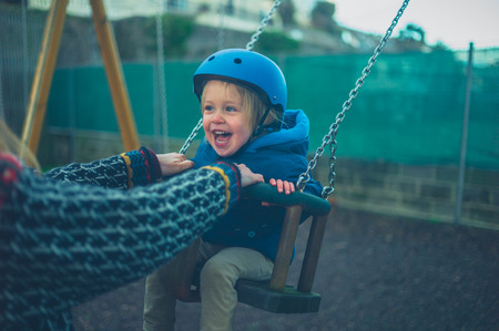 A little toddler wearing a helmet is on the swing in the playgroundの写真素材