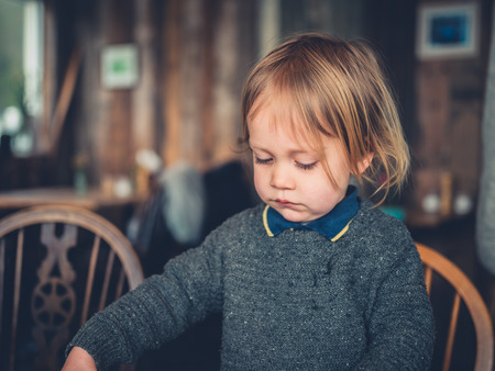 A little toddler is sitting at a table in a cafeの写真素材