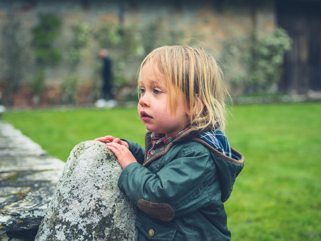 A little toddler is standing on the lawn by an old farmhouseの写真素材