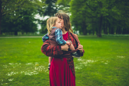 A young mother is visiting a country park and is putting her toddler into a slingの写真素材