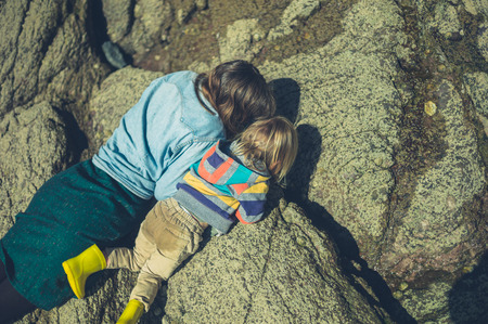 A young mother and her toddler are exploring the rocks on a beachの写真素材
