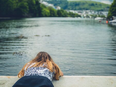 A young woman is lying by a river and looking at the waterの写真素材
