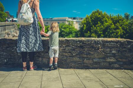 A young mother and her toddler are standing by a stone wall in the summerの写真素材
