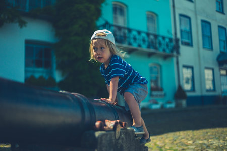 A little toddler is climbing on an old cannon in a seaside town