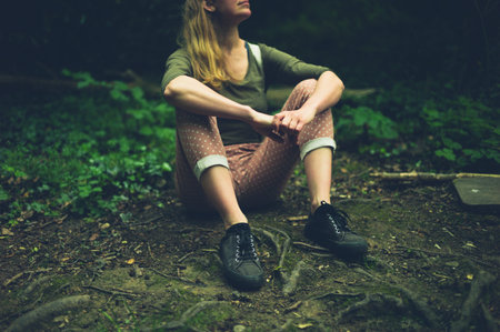 A young woman is sitting on the ground relaxing in the woods