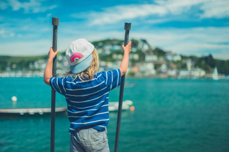 A little toddler is holding onto some railings in a small town by the river
