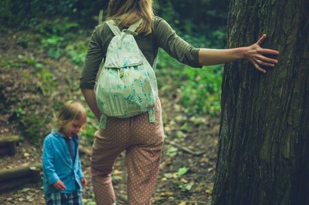 A young mother and her toddler are relaxing by a tree in the woodsの写真素材