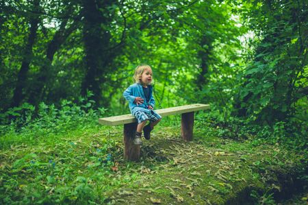 A littlte toddler is sitting by himself on a bench in the woodsの写真素材