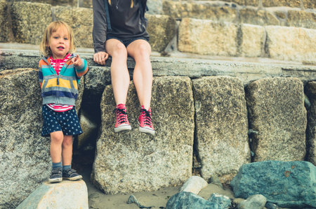 A young woman and a little toddler are relaxing on some rocks outside