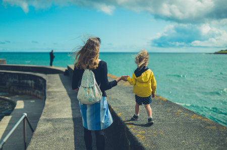 A young mother and her toddler are wealking on a pier by the sea in summer