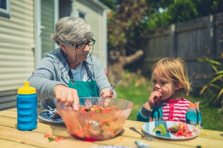 A little toddler and his grandmother are eating lunch outside their caravan in the trailer parkの写真素材