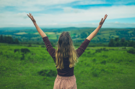 A young woman is raising her arms up in the air on the moor in summer