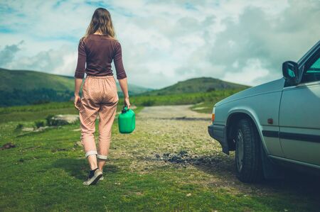 A young woman with a broken down car in nature is off looking for a gas stationの写真素材