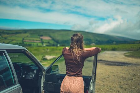 A young woman is relaxing by her car on the moor in summerの写真素材