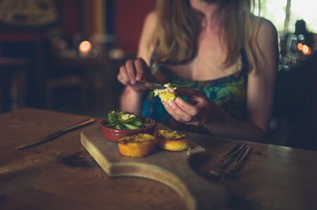 A young woman is eating her dinner in a restaurant, putting pate on a slice of breadの写真素材