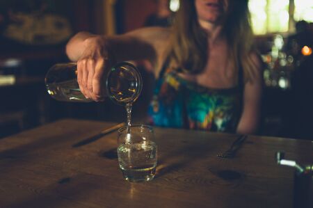 A young woman is pouring herself a glass of water in a restaurantの写真素材
