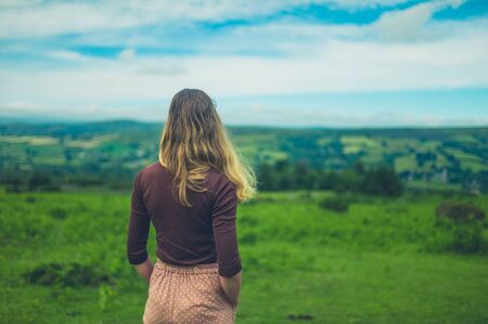 A young woman is looking at a green landscape with hills in the summerの写真素材
