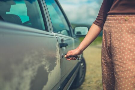A young woman is unlocking her car in nature on a summer dayの写真素材